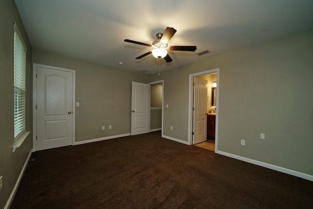 unfurnished bedroom featuring dark colored carpet, ensuite bath, and ceiling fan