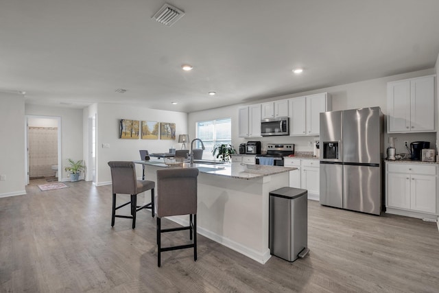 kitchen with white cabinetry, a center island with sink, stainless steel appliances, light stone counters, and sink