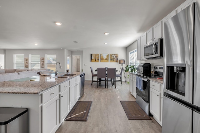 kitchen featuring light stone countertops, white cabinetry, stainless steel appliances, sink, and a center island with sink