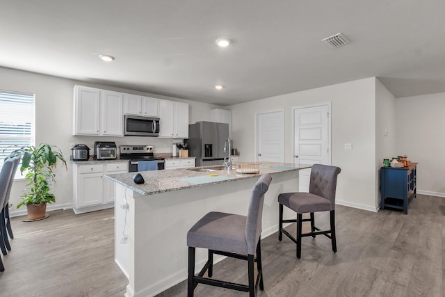 kitchen with light hardwood / wood-style floors, a kitchen bar, appliances with stainless steel finishes, a kitchen island with sink, and white cabinets