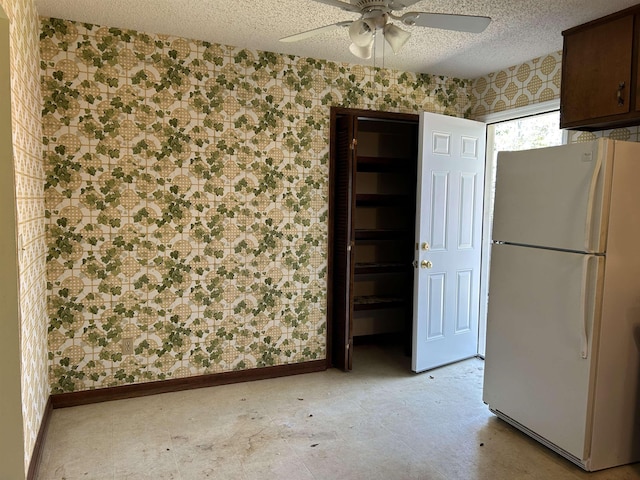 interior space with freestanding refrigerator, wallpapered walls, a ceiling fan, and a textured ceiling