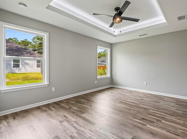 spare room with ceiling fan, a wealth of natural light, wood-type flooring, and a tray ceiling