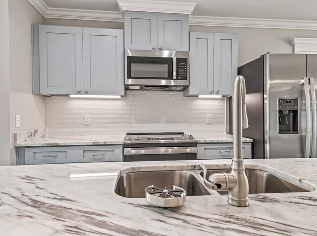 kitchen with crown molding, stainless steel appliances, light stone counters, and gray cabinetry