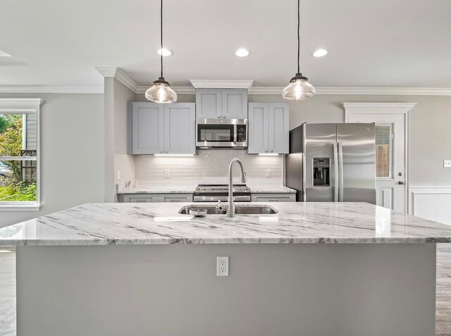 kitchen featuring an island with sink, appliances with stainless steel finishes, light stone counters, and ornamental molding