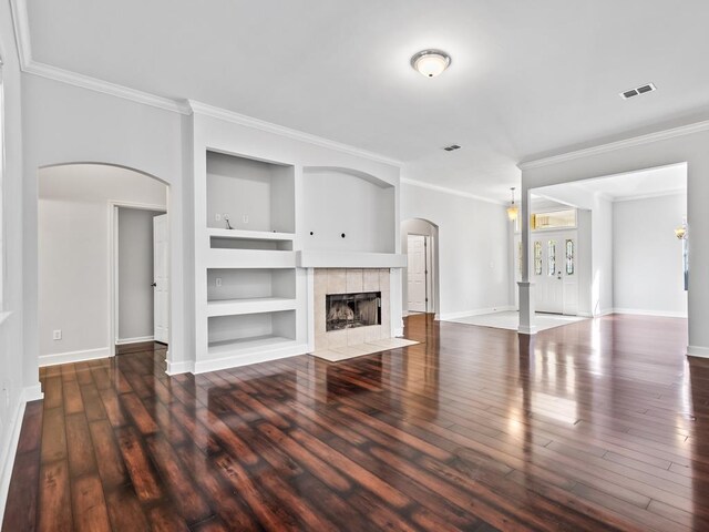 unfurnished living room with a fireplace, built in shelves, crown molding, and dark wood-type flooring