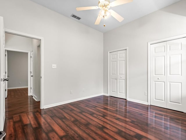 unfurnished bedroom featuring multiple closets, ceiling fan, and dark hardwood / wood-style floors