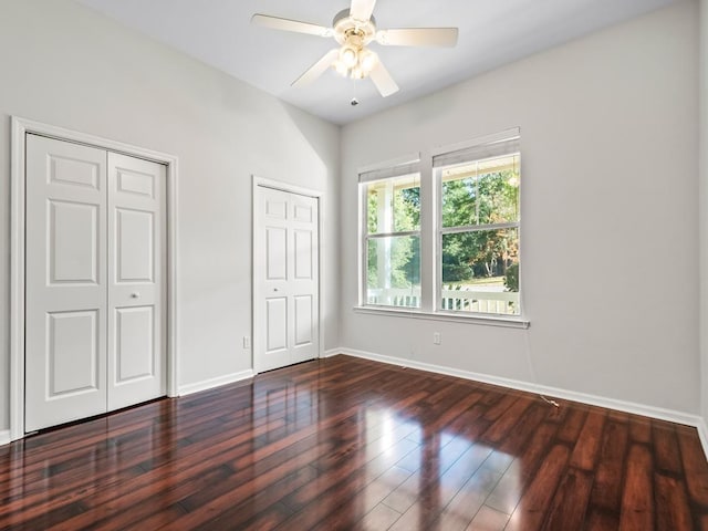 unfurnished bedroom with ceiling fan, dark hardwood / wood-style flooring, and multiple closets