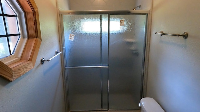 bathroom with toilet, a shower with door, and a healthy amount of sunlight