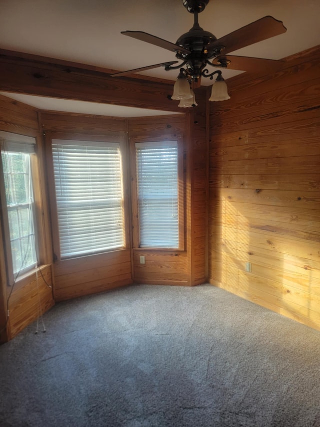 carpeted spare room featuring beamed ceiling, ceiling fan, and wood walls
