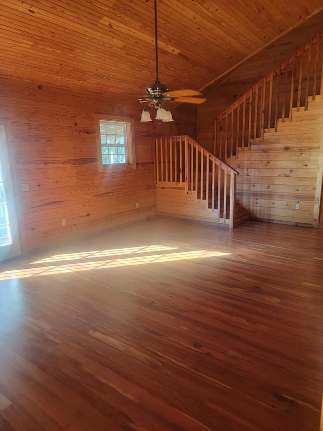 unfurnished living room with wood-type flooring, ceiling fan, wooden ceiling, and wood walls