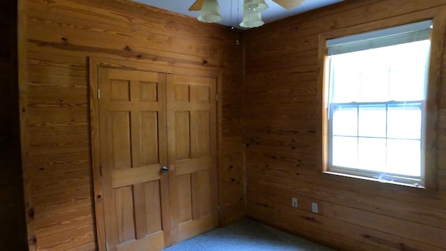 unfurnished bedroom with ceiling fan, wooden walls, and carpet