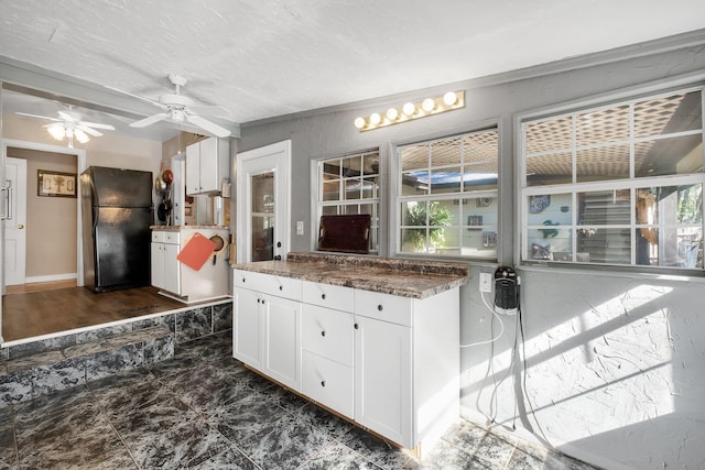 kitchen with white cabinets, dark stone countertops, a textured ceiling, and black fridge