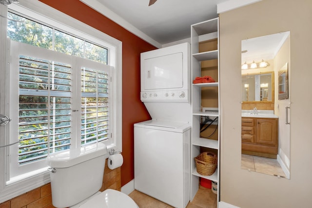 laundry room featuring a healthy amount of sunlight, stacked washer and dryer, sink, and light tile patterned floors