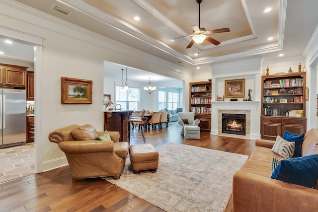 living room with hardwood / wood-style floors, a fireplace, ornamental molding, and a raised ceiling