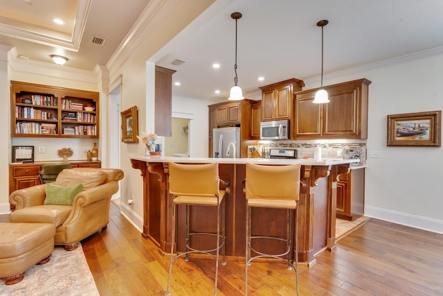 kitchen featuring appliances with stainless steel finishes, light wood-type flooring, a kitchen bar, and decorative light fixtures