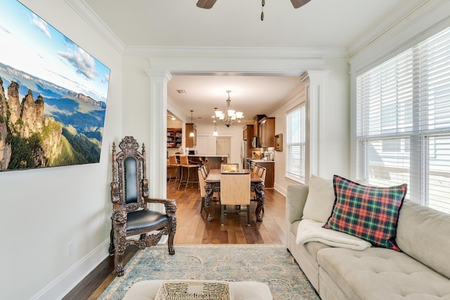 living room with decorative columns, crown molding, ceiling fan with notable chandelier, and light wood-type flooring