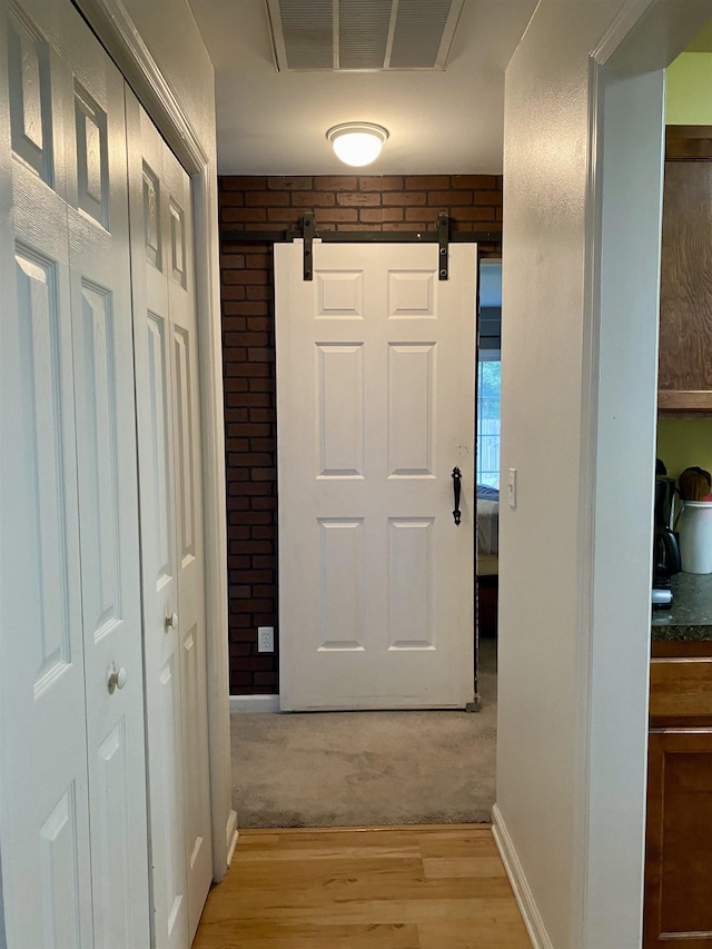 hallway with brick wall, light hardwood / wood-style flooring, and a barn door