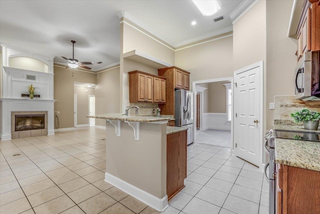 kitchen featuring a breakfast bar area, light stone counters, light tile patterned floors, ornamental molding, and appliances with stainless steel finishes