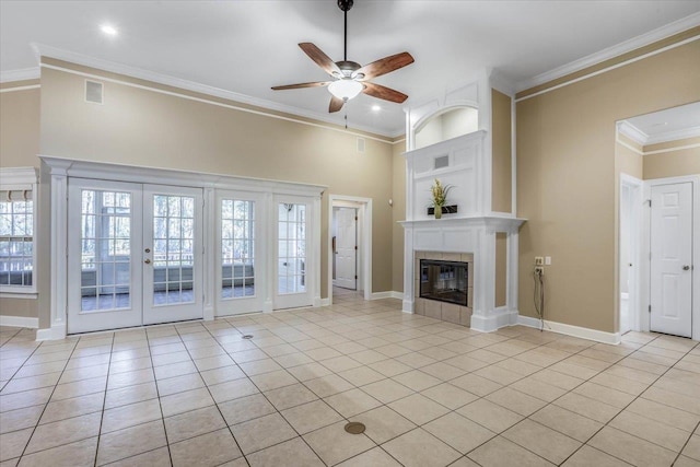 unfurnished living room with light tile patterned floors, crown molding, a tile fireplace, ceiling fan, and french doors