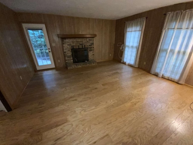 unfurnished living room with wood walls, light hardwood / wood-style floors, a brick fireplace, and a wealth of natural light