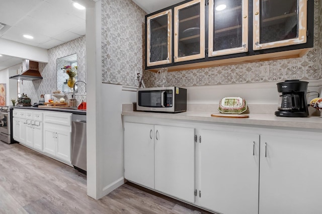 5902 Shady Rest Rd, Havana, FL 32333 - kitchen featuring appliances with stainless steel finishes, wall chimney range hood, light wood finished floors, a sink, and glass insert cabinets