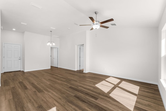 spare room with ceiling fan with notable chandelier, vaulted ceiling, and dark wood-type flooring