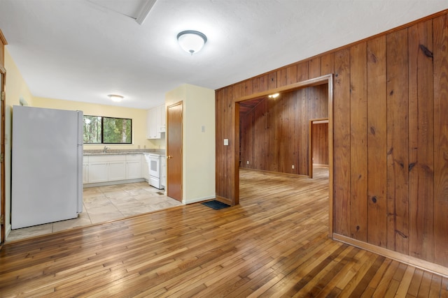 kitchen featuring white cabinets, light hardwood / wood-style flooring, wooden walls, and white appliances