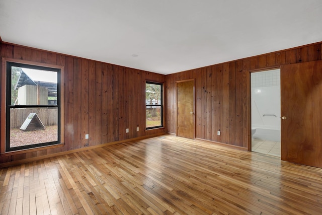 unfurnished room with wood walls, a wealth of natural light, and light hardwood / wood-style floors