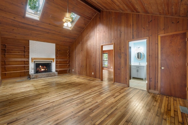 unfurnished living room featuring a brick fireplace, light hardwood / wood-style floors, wood ceiling, high vaulted ceiling, and a skylight
