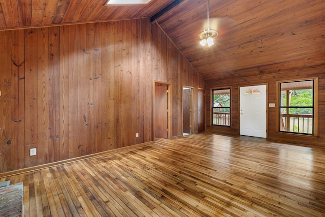 unfurnished living room featuring lofted ceiling with skylight, wood walls, and light wood-type flooring