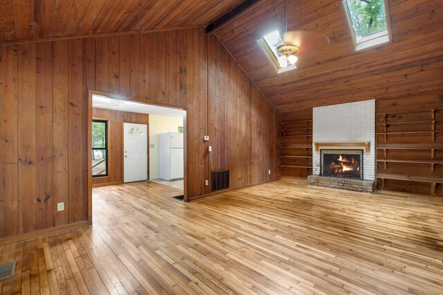 unfurnished living room featuring wood walls, light hardwood / wood-style flooring, lofted ceiling with skylight, and a brick fireplace