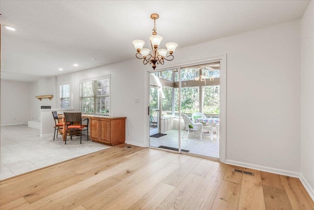 unfurnished dining area with light wood-type flooring, a brick fireplace, baseboards, and visible vents