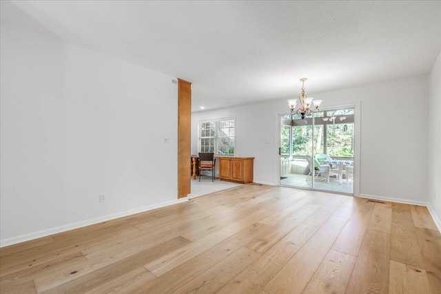 empty room featuring baseboards, light wood-type flooring, and an inviting chandelier