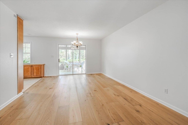 unfurnished room with a chandelier, a wealth of natural light, light wood-style flooring, and baseboards