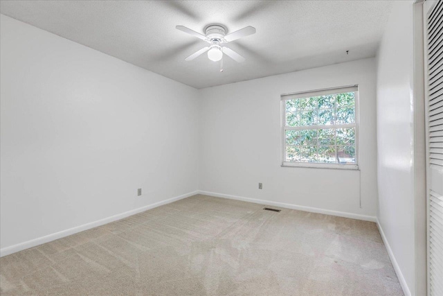 carpeted empty room featuring a textured ceiling, a ceiling fan, visible vents, and baseboards