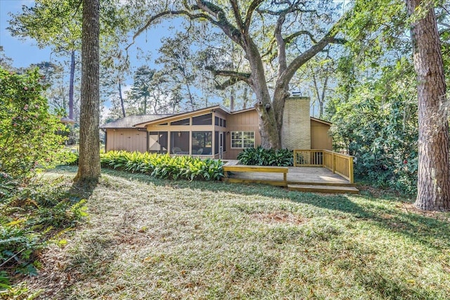 back of property with a sunroom, a chimney, a deck, and a lawn