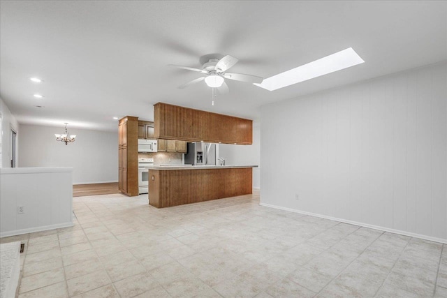 kitchen with a skylight, brown cabinets, open floor plan, white appliances, and ceiling fan with notable chandelier