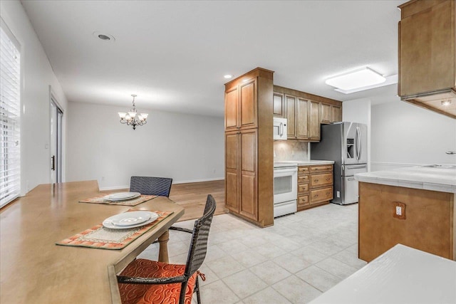 kitchen with a notable chandelier, light countertops, backsplash, brown cabinetry, and white appliances