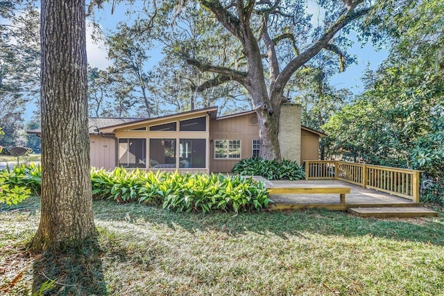 back of property featuring a sunroom, a chimney, a deck, and a yard