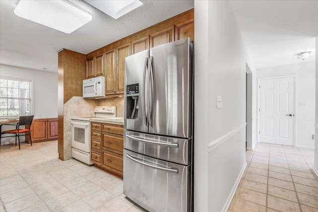 kitchen with a wainscoted wall, tasteful backsplash, light countertops, brown cabinetry, and white appliances