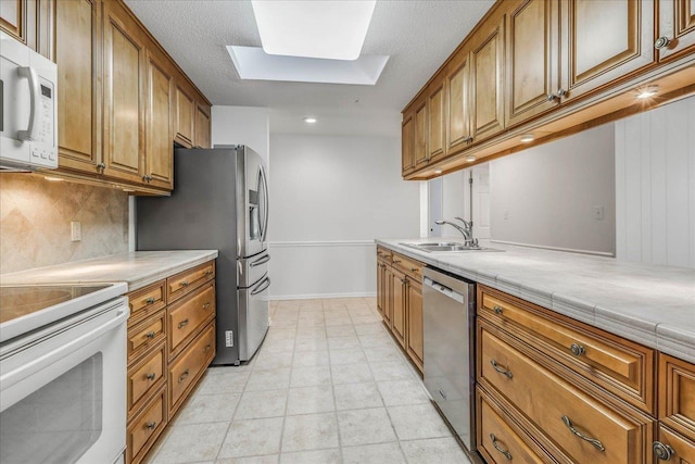 kitchen with a skylight, appliances with stainless steel finishes, brown cabinets, a sink, and backsplash