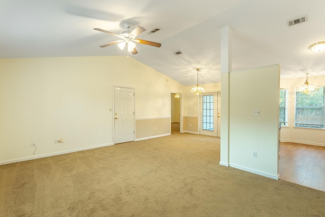 spare room with lofted ceiling, ceiling fan with notable chandelier, and light colored carpet