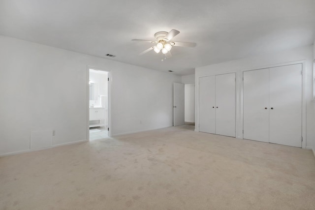 unfurnished bedroom with two closets, light colored carpet, ceiling fan, and ensuite bathroom