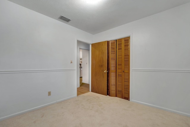 unfurnished bedroom featuring a textured ceiling, light carpet, and a closet