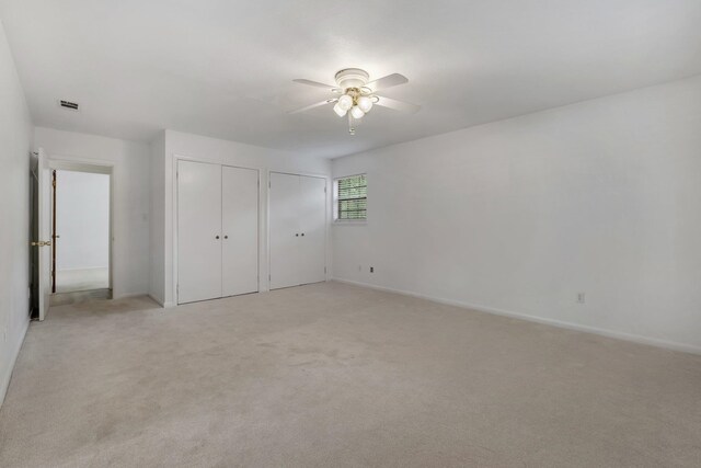 unfurnished bedroom with ceiling fan, light carpet, and multiple closets