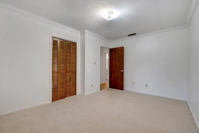 unfurnished bedroom with light colored carpet, a textured ceiling, crown molding, and a closet