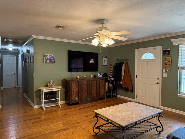 living room featuring baseboards, wood finished floors, visible vents, and ornamental molding