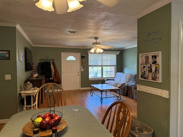 dining area featuring visible vents, ornamental molding, a ceiling fan, wood finished floors, and baseboards