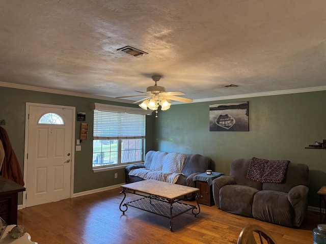 living room with visible vents, a textured ceiling, wood finished floors, crown molding, and baseboards