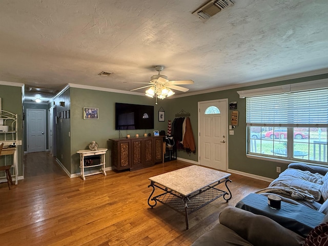 living room featuring visible vents, ornamental molding, a textured ceiling, and wood finished floors